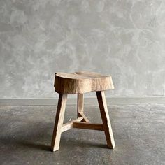 a wooden stool sitting on top of a cement floor next to a wall with a concrete background