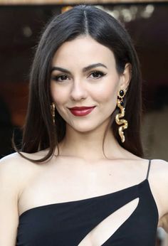 a woman with long dark hair wearing gold earrings and black dress smiling at the camera