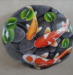 a painted rock with two koi fish and green leaves on the top is shown