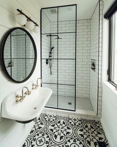 a black and white tiled bathroom with a walk in shower next to a sink under a round mirror