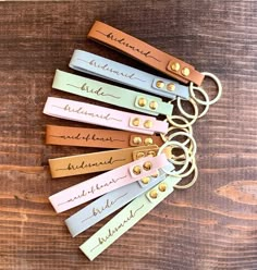 leather keychains with name tags on them sitting on a wooden surface, all in different colors