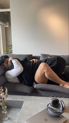 a man laying on top of a gray couch next to a vase with flowers in it