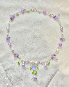 this handmade purple flowering forest necklace is handmade using mixed clear, white, purple and green glass, stone and plastic beads and pearls and features flowers, hand-wrapped leafy accents and a pendant in its center.  please don't hesitate to message me with any questions :) Purple Jewelry Aesthetic, Purple And Green Aesthetic, Beaded Necklace Aesthetic, Cottage Core Ideas, Bead Fairy, Cottage Core Jewelry, Purple Beaded Necklace, Core Ideas, Diy Choker