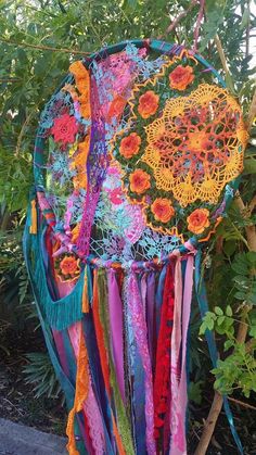 a multicolored piece of art hanging from a tree in the sun with flowers on it