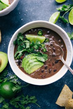 a bowl of black bean soup with avocado and cilantro on the side