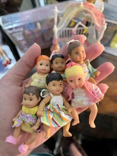 a hand holding a small group of little dolls in it's palm, next to a pile of other toys