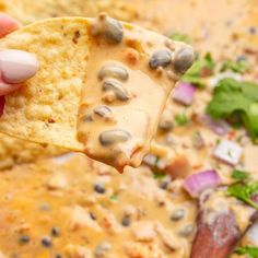 a hand holding a tortilla chip over a bowl of quesadilla soup