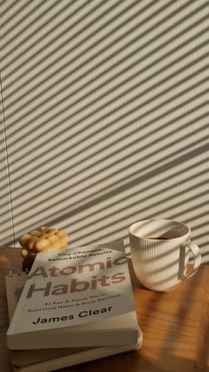 a stack of books sitting on top of a wooden table next to a cup of coffee