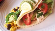 two tacos on a plate with corn and tomatoes