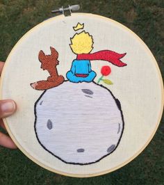 someone is holding up a small embroidery art piece with a little boy sitting on top of it