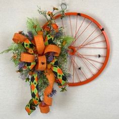 a bicycle wheel decorated with orange and green flowers on the wall next to a wreath