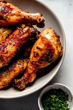 grilled chicken legs on a white plate with parsley next to it and a small bowl of seasoning