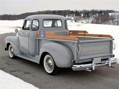 an old gray truck parked on the side of a road next to snow covered ground