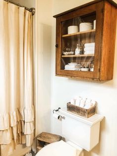 a white toilet sitting next to a wooden cabinet in a bathroom under a shower curtain