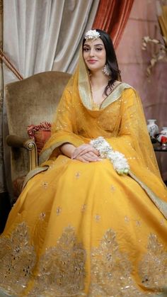 a woman sitting in a chair wearing a yellow dress with gold trims and flowers on her head