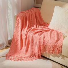 an orange blanket sitting on top of a couch next to a white pillow and window