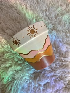 a cup that is sitting on top of a rug in the sun and has some designs on it