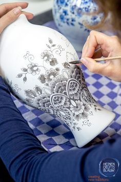 a woman is painting a vase with black and white designs