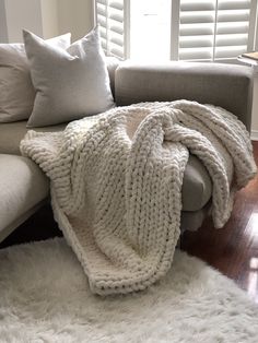 a white blanket sitting on top of a couch in a living room next to pillows