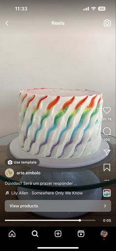 a white cake with rainbow icing sitting on top of a glass table next to a cell phone