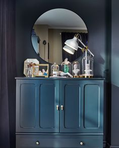 a blue dresser with a mirror and lights on it in a room that has black walls