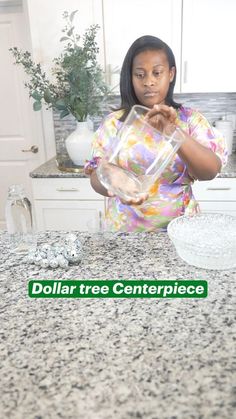 a woman standing in front of a counter holding a glass container with the words dollar tree centerpiece on it