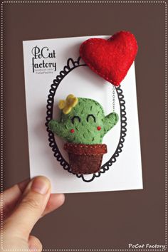 a small green cactus with a red heart on it's head sitting on top of a piece of paper