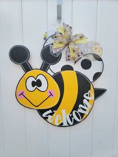 a yellow and black bee door hanger on the side of a white door with a bow