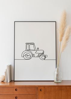 a drawing of a tractor on a white wall next to a wooden dresser and vase with dry grass in it