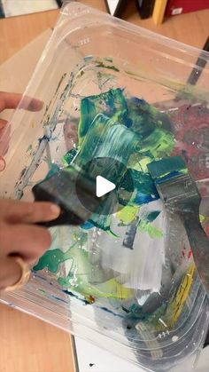 someone is using scissors to paint on an object in a plastic container with watercolors