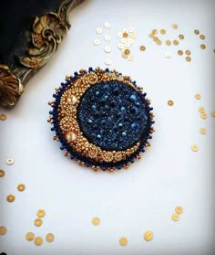 a blue and gold beaded brooch sitting on top of a piece of cloth