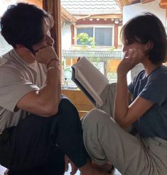 a man and woman sitting next to each other on the floor with an open book in front of them