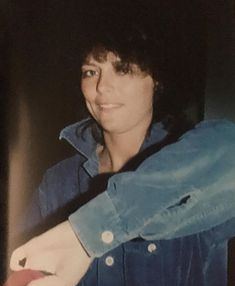 a woman is holding something in her hand and smiling at the camera while wearing a denim shirt