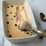 a scoop of ice cream in a white bowl with chocolate chips on it and spoons