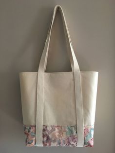 a white bag hanging on the wall with a pink flowered design and two handles