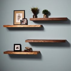 three wooden shelves with pictures on them against a blue wall, one has a potted plant and the other two are empty