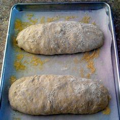 two loaves of bread sitting on top of a baking pan covered in flour and seasoning