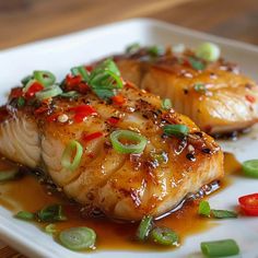 two pieces of fish on a white plate with sauce and green onion garnish