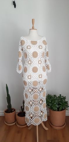 a white crocheted dress sitting on top of a wooden table next to potted plants