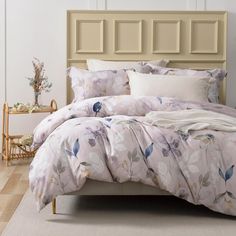 a bed with white and blue flowers on it in a room next to a beige headboard