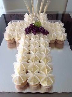 a cross made out of cupcakes on top of a white tablecloth with purple flowers