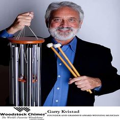 a man holding two wooden mallets next to a wind chime