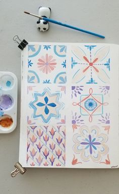 an open notebook with watercolors and paint next to it on top of a table