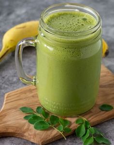 a green smoothie in a mason jar on a cutting board next to a banana