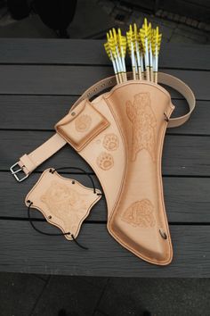 a leather case with arrows in it sitting on a wooden table next to other items