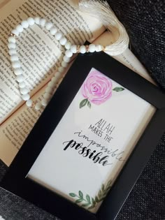 an open book with a pink rose on it next to a white beaded necklace