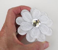 a hand holding a crystal flower brooch with white petals and clear crystals on it