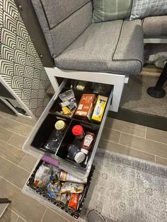 an open drawer in the floor next to a couch with food and condiments