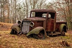 an old rusted out truck sitting in the woods