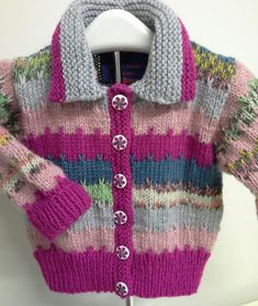 a pink and grey knitted sweater with buttons on the front, attached to a white coat hanger